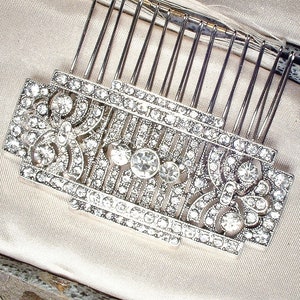 May include: A silver hair comb with a decorative design of clear rhinestones. The comb has a rectangular shape and is adorned with intricate patterns.
