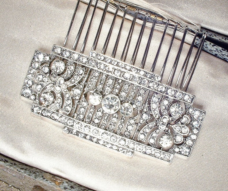 May include: A silver hair comb with a decorative design of clear rhinestones. The comb has a rectangular shape and is adorned with intricate patterns.