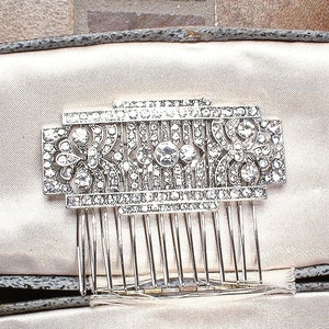 May include: A silver hair comb with a decorative design of clear rhinestones. The comb is in a white velvet box.