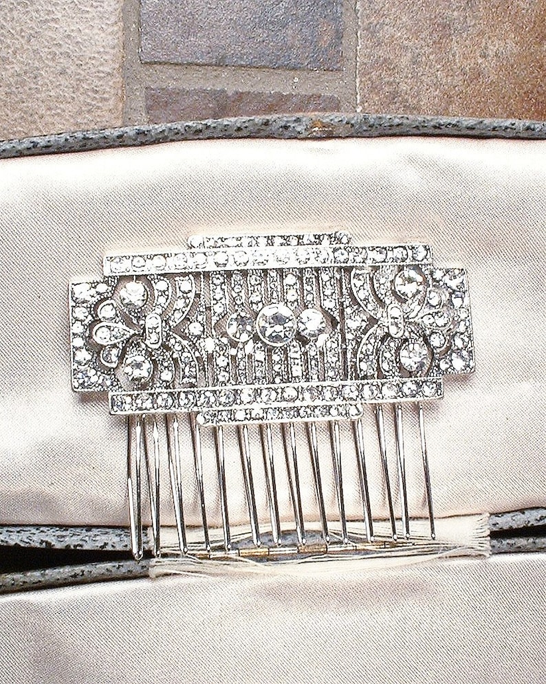 May include: A silver hair comb with a decorative design of clear rhinestones. The comb is in a white velvet box.
