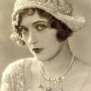 Pu&ograve; includere: Un ritratto in bianco e nero di una donna che indossa un cappello e una collana di perle. La donna guarda la fotocamera e ha un'espressione seria sul viso. Il testo "Amore Treasure" &egrave; scritto in corsivo nella parte inferiore dell'immagine.