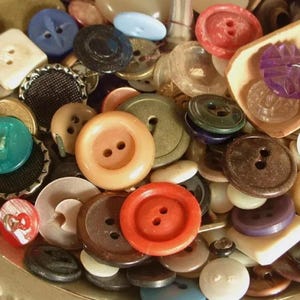 May include: A collection of assorted buttons in various colours, shapes, and sizes. The buttons are made of different materials, including plastic, metal, and fabric. Some of the buttons have two holes, while others have four holes. There are also some buttons with decorative designs.