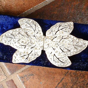 Peut inclure: Une broche argent&eacute;e en forme de feuille avec des d&eacute;tails complexes, pos&eacute;e sur un fond en velours bleu fonc&eacute;. La broche pr&eacute;sente un motif d&eacute;licat de veines et est orn&eacute;e de petits accents scintillants.