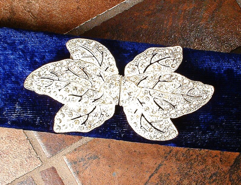Peut inclure: Une broche argent&eacute;e en forme de feuille avec des d&eacute;tails complexes, pos&eacute;e sur un fond en velours bleu fonc&eacute;. La broche pr&eacute;sente un motif d&eacute;licat de veines et est orn&eacute;e de petits accents scintillants.