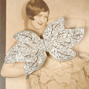 Peut inclure: Broche argent&eacute;e vintage en forme de feuille ou de n&oelig;ud, orn&eacute;e de petites pierres scintillantes. La broche pr&eacute;sente des d&eacute;tails de veines d&eacute;licats. Le fond est une photographie s&eacute;pia d'une femme.
