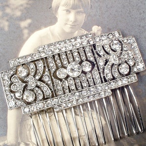 May include: A silver hair comb with a decorative design of clear rhinestones. The comb has a geometric pattern with a floral motif.
