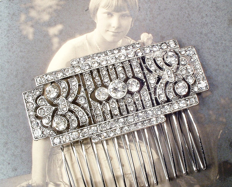 May include: A silver hair comb with a decorative design of clear rhinestones. The comb has a geometric pattern with a floral motif.