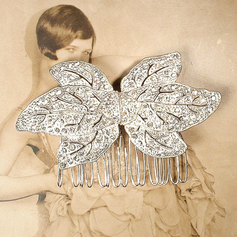 Peut inclure: Un peigne &agrave; cheveux argent&eacute; avec un grand n&oelig;ud ornemental. Le n&oelig;ud est orn&eacute; de strass &eacute;tincelants, et le peigne comporte plusieurs dents. Le fond est une photographie s&eacute;pia d'une femme.