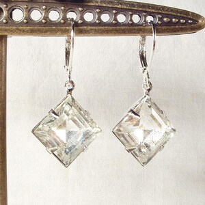Puede incluir: Un par de pendientes de cristal transparente y facetado con forma cuadrada de diamante. Los pendientes est&aacute;n suspendidos de cierres de palanca plateados. Los pendientes se exhiben en un soporte met&aacute;lico decorativo.