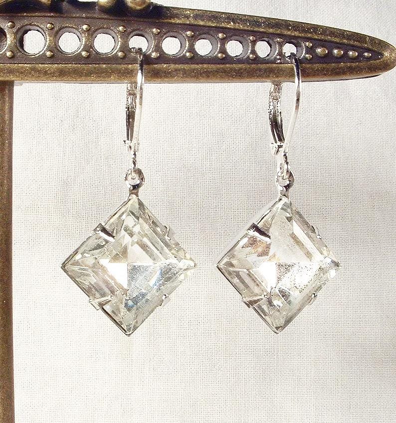 Puede incluir: Un par de pendientes de cristal transparente y facetado con forma cuadrada de diamante. Los pendientes est&aacute;n suspendidos de cierres de palanca plateados. Los pendientes se exhiben en un soporte met&aacute;lico decorativo.