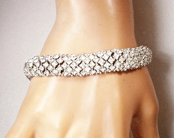 May include: A sparkling silver bracelet with a lattice design, set with numerous clear, round-cut rhinestones. The bracelet is shown on a person's wrist, showcasing its intricate pattern and reflective qualities. This piece of jewelry is suitable for special occasions.
