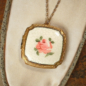 May include: A gold locket necklace with a white enamel square pendant featuring a hand-painted pink rose with green leaves.