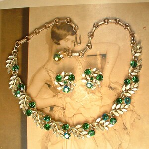 May include: A vintage jewelry set featuring a necklace and matching earrings. The necklace and earrings have a gold-tone metal leaf design, adorned with green and blue-green gemstones. The necklace is connected with a chain and clasp.