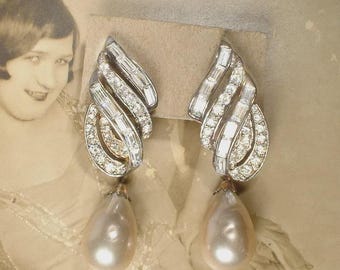 May include: A pair of silver-toned earrings featuring a curved, fan-like top section encrusted with clear baguette and round cut stones. Each earring terminates in a large, smooth, teardrop-shaped white pearl that hangs from the decorative metal base.