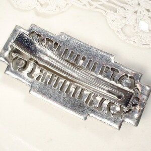 May include: Silver-toned hair clip with an intricate geometric design. The clip has a spring-loaded mechanism and a smooth, polished finish.