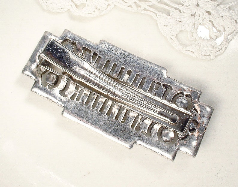 May include: Silver-toned hair clip with an intricate geometric design. The clip has a spring-loaded mechanism and a smooth, polished finish.