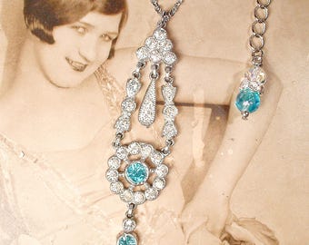 Puede incluir: Un collar plateado con un colgante adornado con pedrería transparente y turquesa. El colgante presenta un diseño floral con una piedra central turquesa y una piedra turquesa más pequeña en la parte inferior. También se ve un segundo collar con una cuenta turquesa.