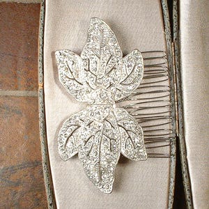 Peut inclure: Un peigne &agrave; cheveux argent&eacute; orn&eacute; d'une feuille incrust&eacute;e de strass &eacute;tincelants. Le peigne est dot&eacute; de dents m&eacute;talliques pour la fixation. Pr&eacute;sent&eacute; dans un &eacute;crin aux tons neutres, il sugg&egrave;re un accessoire vintage ou de c&eacute;r&eacute;monie, avec un design d&eacute;taill&eacute;.