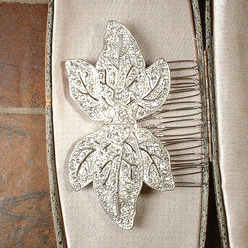 Peut inclure: Un peigne &agrave; cheveux argent&eacute; orn&eacute; d'une feuille incrust&eacute;e de strass &eacute;tincelants. Le peigne est dot&eacute; de dents m&eacute;talliques pour la fixation. Pr&eacute;sent&eacute; dans un &eacute;crin aux tons neutres, il sugg&egrave;re un accessoire vintage ou de c&eacute;r&eacute;monie, avec un design d&eacute;taill&eacute;.