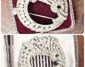 May include: A silver-toned circular hair accessory and brooch set featuring intricate metalwork encrusted with clear rhinestones. The circular design includes curved, layered patterns and a pin mechanism on the back of the brooch, while the hair comb features a matching decorative top.