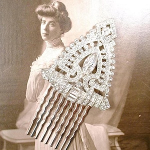 May include: A silver-toned hair comb featuring a triangular decorative top encrusted with numerous clear, sparkling rhinestones. The design includes a central marquise-cut stone and a series of smaller round stones arranged in a geometric pattern.