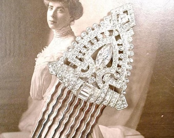 May include: A silver-toned hair comb featuring a triangular decorative top encrusted with numerous clear, sparkling rhinestones. The design includes a central marquise-cut stone and a series of smaller round stones arranged in a geometric pattern.