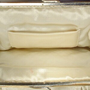May include: An open rectangular clutch bag featuring a metallic gold-tone frame with a hinged clasp closure. The interior is lined with smooth cream-colored satin fabric and includes a single horizontal slip pocket along the back wall.