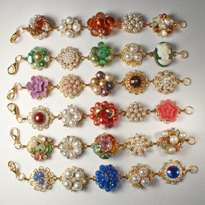 May include: A collection of decorative bracelets with floral and gem designs. Each bracelet features a series of ornate, flower-shaped centerpieces in various colors, including red, pink, green, and blue, connected by gold-toned chains and clasps.