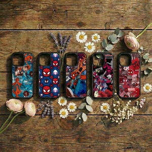 Könnte beinhalten: Fünf Handyhüllen mit Spider-Man-Designs werden auf einer Holzoberfläche präsentiert. Die Hüllen zeigen verschiedene farbenfrohe Grafiken, darunter Comic-Kunst und das Spider-Man-Logo. Florale Akzente umgeben die Hüllen.