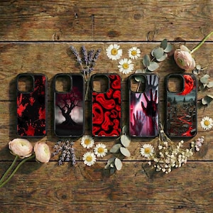 May include: Five black phone cases with unique designs. The cases feature images of a bloody hand, a tree, red abstract patterns, a hand reaching out, and a cemetery scene. The cases are arranged on a wooden surface with flowers and greenery.