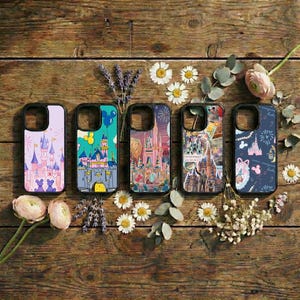 Könnte beinhalten: Fünf Handyhüllen mit farbenfrohen Schlossdesigns sind auf einer Holzoberfläche mit Blumen angeordnet. Die Hüllen zeigen verschiedene Illustrationen von Schlössern, Luftballons und Feuerwerk. Die Hüllen sind in den Farbtönen Lila, Blau, Rosa und Gelb gehalten.
