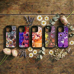 May include: Five phone cases with black borders, each featuring a different colorful design from the Five Nights at Freddy's franchise. The cases are arranged on a rustic wooden surface, surrounded by flowers and greenery.