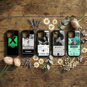 May include: Five black phone cases with different designs and text, including a green "X" and the words "Teenagers My Chemical Romance." The cases are displayed on a wooden surface with flowers and greenery.