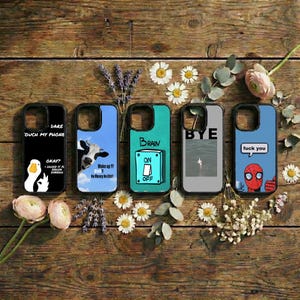 May include: Five phone cases with various designs and text. The cases are black, blue, teal, and gray. One case says "DARE OUCH MY PHONE" with a duck graphic. Another has a cow graphic and says "Wake up!!! No Money No Life!!". The third says "BRAIN ON OFF". The fourth says "BYE". The last one has a Spiderman graphic and says "fuck you".
