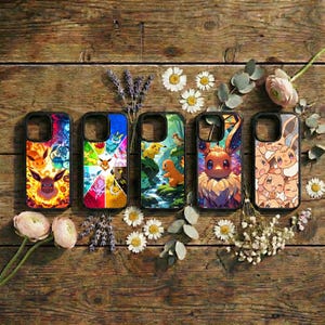 May include: Five black phone cases with colorful illustrations of Pokémon characters. The cases are arranged on a rustic wooden surface, surrounded by flowers and sprigs of lavender. Each case features a different design, showcasing various Pokémon.