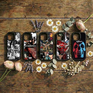 Könnte beinhalten: Fünf schwarze Handyhüllen mit einzigartigen Designs, die Collagen, Albumcover und den Bandnamen "Deftones" zeigen. Die Hüllen sind auf einer rustikalen Holzoberfläche angeordnet, die mit Blumen und Grün geschmückt ist.