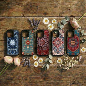 May include: Five phone cases with intricate, colorful patterns resembling oriental rugs are displayed on a rustic wooden surface. The cases feature a variety of designs in shades of blue, red, and teal, with black borders.