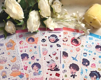 May include: A collection of colorful sticker sheets featuring anime-style character illustrations. Each sheet has a unique design with characters, dates, and themed icons. The sheets are arranged with white flowers and a yellow plush toy in the background.
