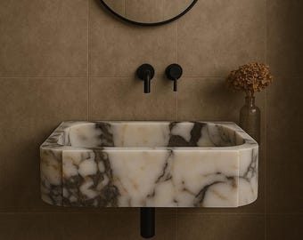 May include: A rectangular marble sink with a black base and faucet fixtures. The sink has a white and brown marbled pattern. A black circular mirror hangs above the sink. A small vase with dried flowers is to the right.
