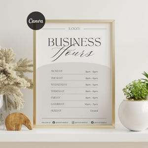 May include: A framed sign displaying business hours, with a gold frame. The sign features the text "BUSINESS Hours" in a stylish script. The opening times for each day are listed. The sign is on a white shelf with decorative items.