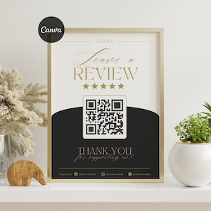 May include: A framed sign with a gold border, featuring the words "Leave a REVIEW" in elegant script above a QR code. The sign also includes the text "THANK YOU for supporting us!" and social media handles.