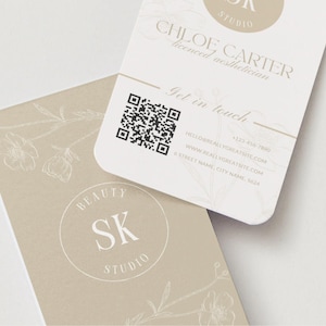 Może przedstawiać: Dwie wizytówki z zaokrąglonymi rogami. Jedna karta jest jasno-beżowa z napisem "BEAUTY SK STUDIO" w okręgu. Druga karta jest biała z napisem "CHLOE CARTER licensed aesthetician" i kodem QR.