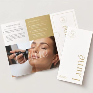 May include: A brochure and two business cards with the word "Lumé" in gold lettering. The brochure is open, displaying text and an image of a woman receiving a facial treatment. The business cards have the "Lumé" logo and text.