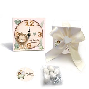 Könnte beinhalten: Eine quadratische, hellrosa Uhr mit einer Löwenillustration, eine weiße Geschenkbox mit cremefarbenem Band, ein Anhänger mit einer Autoillustration und ein kleiner Beutel mit weißen Süßigkeiten. Die Uhr trägt den Text "Il mio Battesimo Leonardo".
