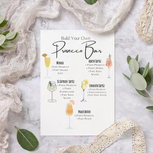 May include: A printable sign with the text "Build Your Own Prosecco Bar" and instructions for making five different cocktails: Mimosa, Aperol Spritz, St. Germain Spritz, Limoncello Spritz, and Peach Bellini.