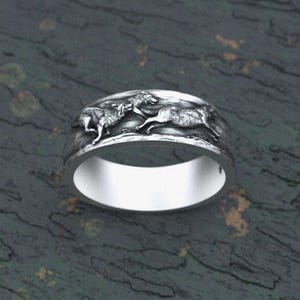 Puede incluir: Un anillo de plata con un diseño de tres lobos corriendo alrededor de la banda.