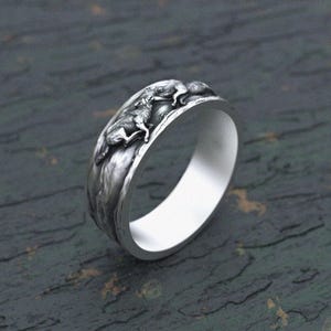 May include: A silver ring featuring a detailed design of two wolves running on a rocky surface.