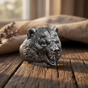 May include: A silver-toned metal ring featuring a detailed, three-dimensional sculpture of a bear head. The bear is depicted with a textured fur finish, pointed ears, and an open mouth showing teeth, creating a realistic and rugged appearance.