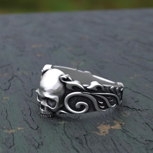 May include: A silver ring with a skull design and intricate floral details. The skull is three-dimensional and has a detailed face.