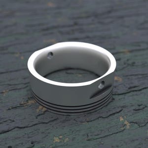 May include: A silver ring with a textured band and two small holes. The ring is made to look like a piston.